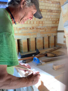 Man in green shirt prepares work outside a kiln.