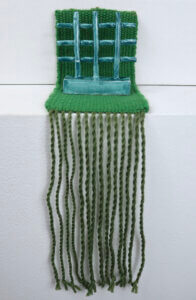 Artwork containing blue-green ceramic lattice piece atop a green woven textile.