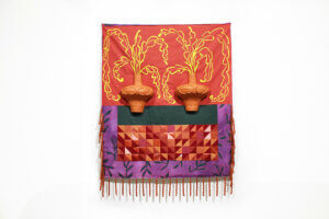Artwork with two ceramic vessels and colorful printed and quilted textile behind it.