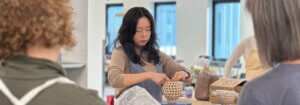 An artist builds a woven ceramic vessel by hand while others watch